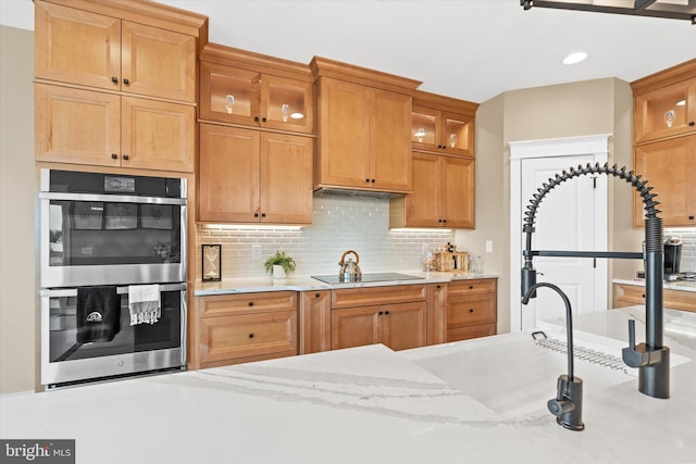 kitchen with backsplash, double oven, black electric cooktop, and light stone counters