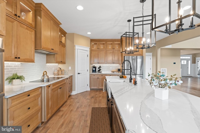 kitchen with black electric stovetop, hanging light fixtures, stainless steel fridge, an inviting chandelier, and light wood-type flooring