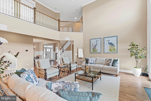 living room with a towering ceiling, crown molding, and light wood-type flooring