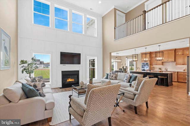 living room featuring ornamental molding, a notable chandelier, light wood-type flooring, and a towering ceiling