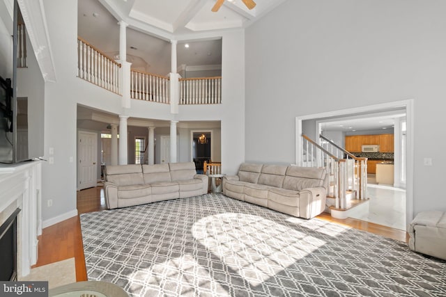 living room with hardwood / wood-style flooring, decorative columns, beamed ceiling, ceiling fan, and a high ceiling