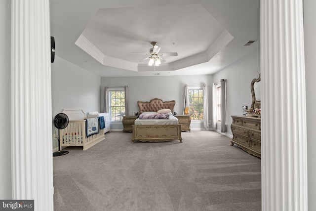 bedroom with light colored carpet, multiple windows, and a tray ceiling