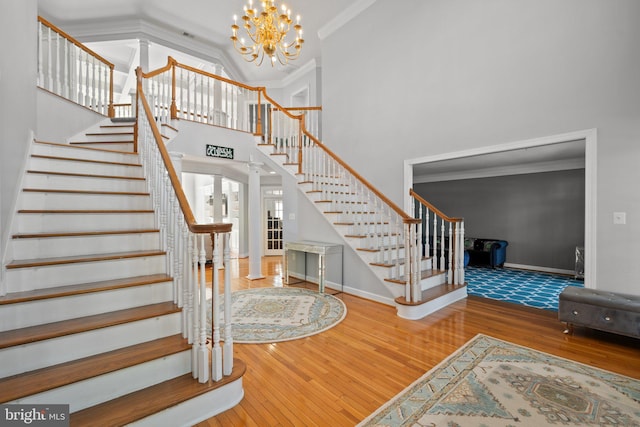 staircase featuring high vaulted ceiling, hardwood / wood-style floors, crown molding, a notable chandelier, and ornate columns