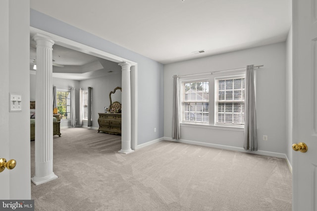 carpeted empty room featuring plenty of natural light, decorative columns, and a tray ceiling