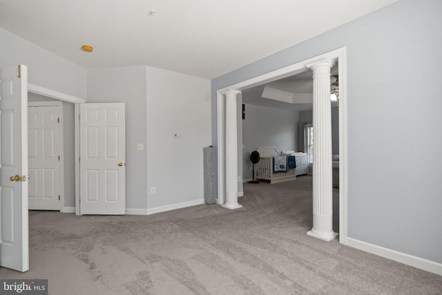 unfurnished bedroom with light colored carpet, a tray ceiling, and decorative columns