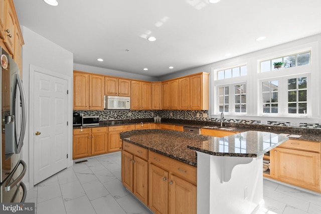 kitchen with decorative backsplash, stainless steel appliances, a kitchen island, and dark stone countertops