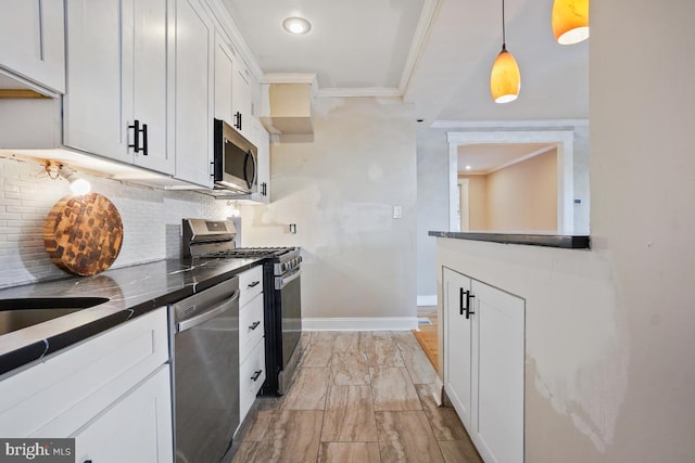 kitchen featuring decorative backsplash, ornamental molding, appliances with stainless steel finishes, decorative light fixtures, and white cabinetry