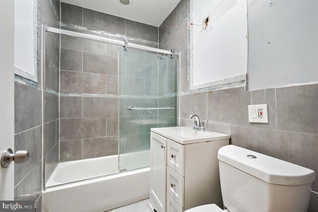 full bathroom featuring vanity, bath / shower combo with glass door, tile walls, and toilet