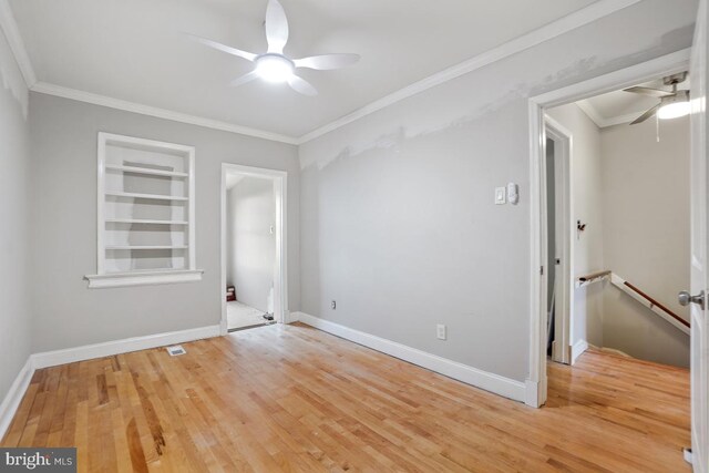 unfurnished room with built in shelves, light hardwood / wood-style floors, and crown molding