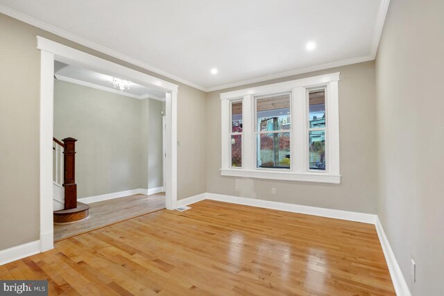 spare room with hardwood / wood-style floors, crown molding, and an inviting chandelier