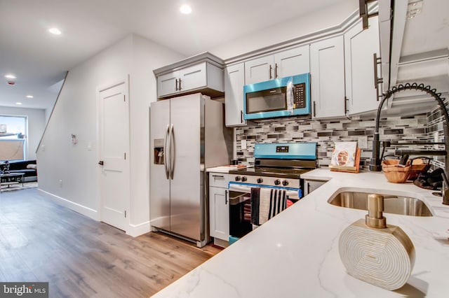 kitchen with backsplash, appliances with stainless steel finishes, light wood-type flooring, light stone countertops, and sink