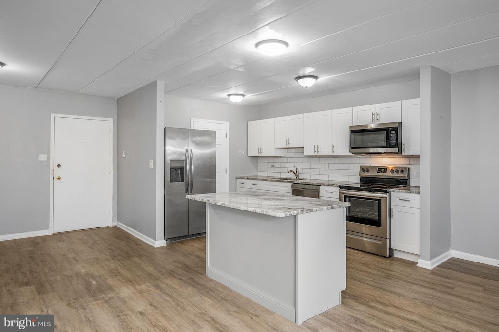 kitchen with tasteful backsplash, appliances with stainless steel finishes, a kitchen island, white cabinetry, and light hardwood / wood-style flooring