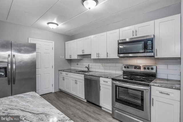 kitchen with hardwood / wood-style floors, white cabinetry, light stone countertops, sink, and stainless steel appliances