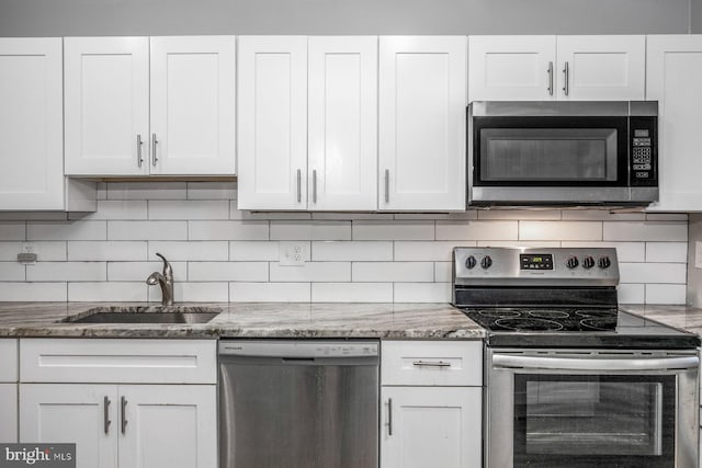 kitchen featuring white cabinets, backsplash, appliances with stainless steel finishes, stone countertops, and sink