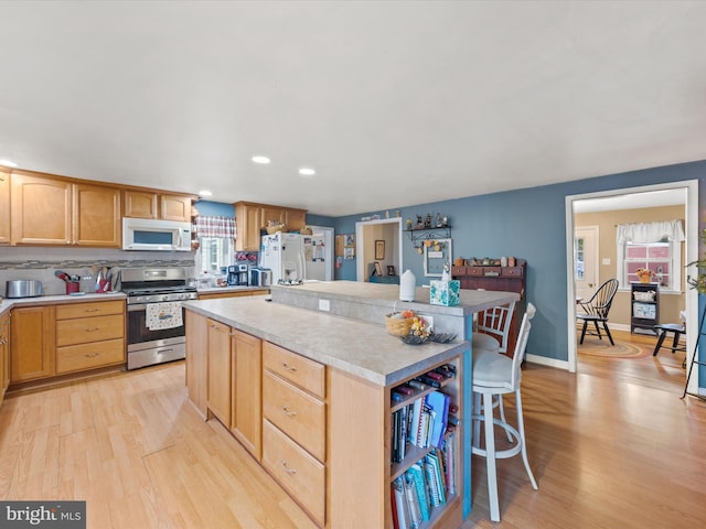 kitchen featuring a kitchen island, light wood-type flooring, decorative backsplash, a breakfast bar, and white appliances