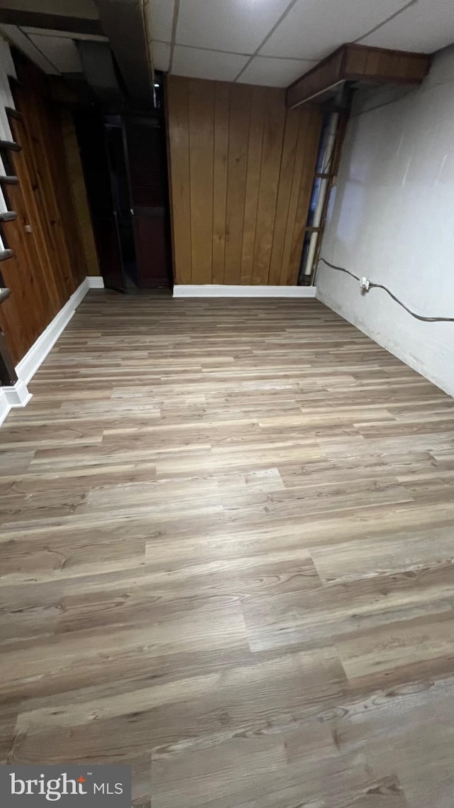 basement with a paneled ceiling, light hardwood / wood-style flooring, and wooden walls