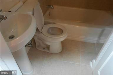 bathroom with a tub to relax in, tile patterned floors, and toilet