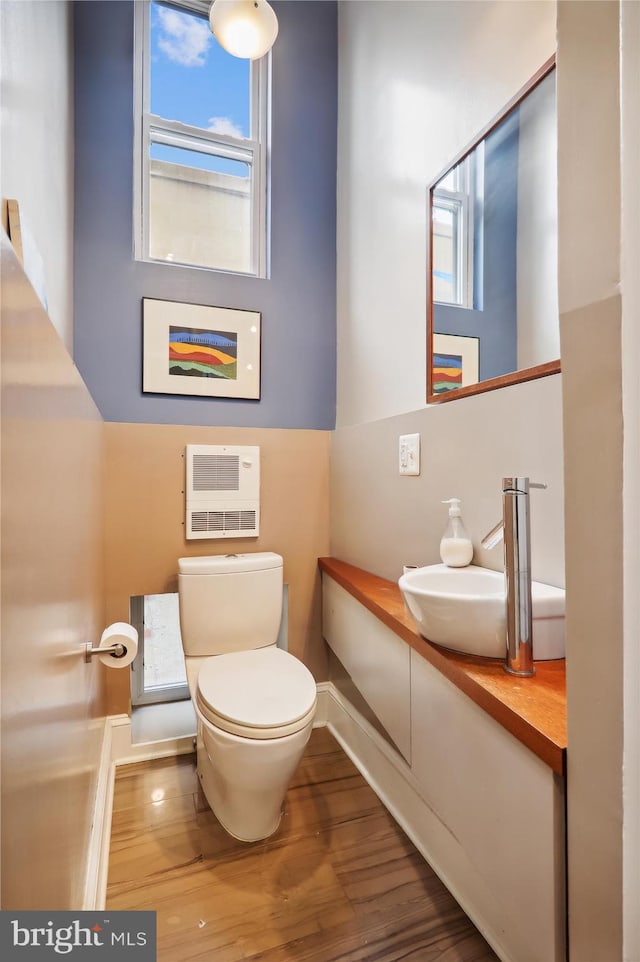 bathroom featuring toilet, heating unit, sink, and hardwood / wood-style flooring