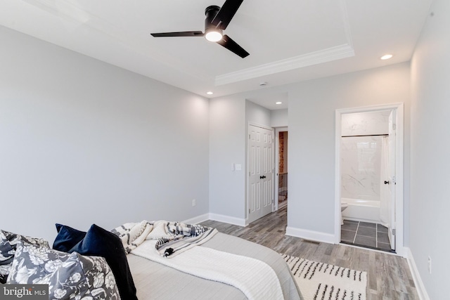 bedroom with light hardwood / wood-style floors, ceiling fan, a tray ceiling, connected bathroom, and a closet