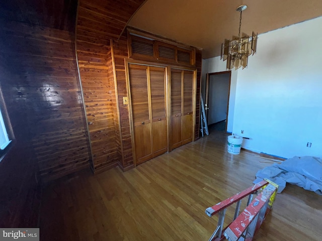 unfurnished bedroom with a closet, wooden walls, dark hardwood / wood-style floors, and an inviting chandelier