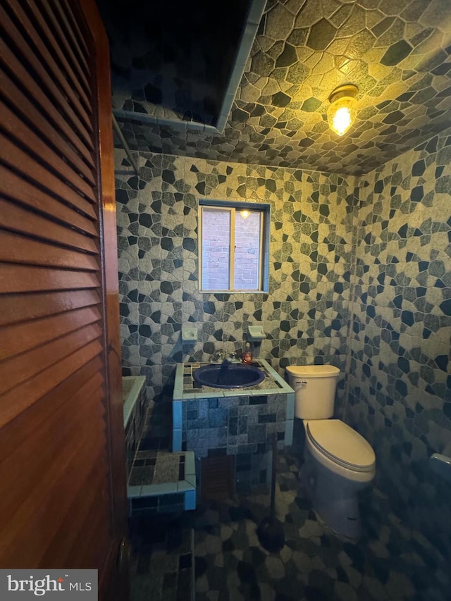 bathroom featuring toilet, tile walls, and sink