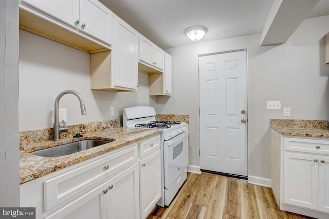 kitchen featuring white gas stove, white cabinetry, sink, light stone counters, and light wood-type flooring