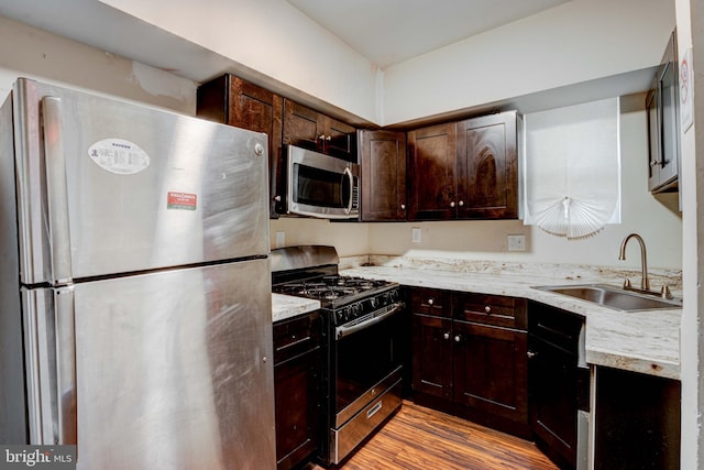 kitchen featuring sink, appliances with stainless steel finishes, light stone countertops, dark brown cabinets, and light wood-type flooring