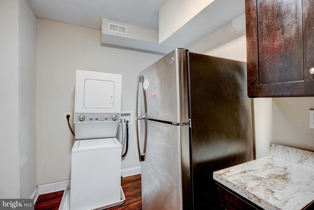 clothes washing area featuring dark hardwood / wood-style floors and stacked washer and clothes dryer