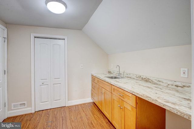 kitchen with light hardwood / wood-style flooring, sink, vaulted ceiling, and light stone countertops