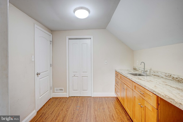 interior space with light wood-type flooring, lofted ceiling, sink, and light stone countertops