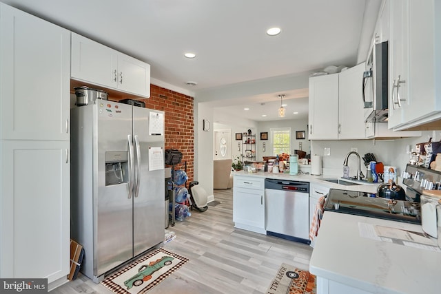 kitchen featuring light wood-type flooring, brick wall, stainless steel appliances, sink, and white cabinetry