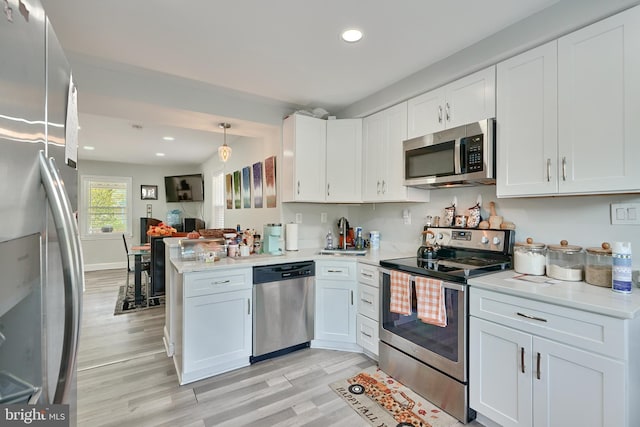 kitchen with kitchen peninsula, white cabinets, stainless steel appliances, and light wood-type flooring