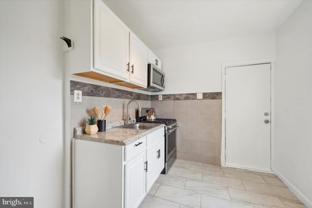 kitchen with white cabinets, light stone countertops, tile walls, stainless steel appliances, and sink