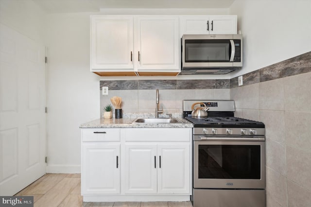 kitchen with white cabinets, stainless steel appliances, sink, and light stone counters