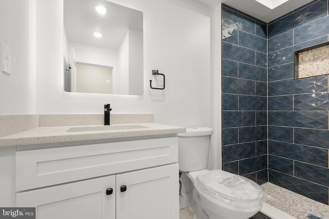 bathroom with a tile shower, vanity, and toilet