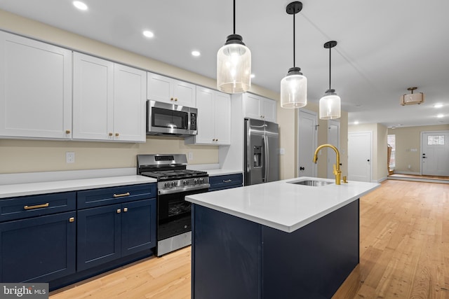 kitchen with sink, stainless steel appliances, pendant lighting, light hardwood / wood-style floors, and a kitchen island with sink