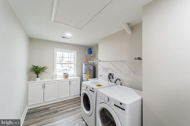 washroom featuring washing machine and clothes dryer, water heater, cabinets, and light hardwood / wood-style floors