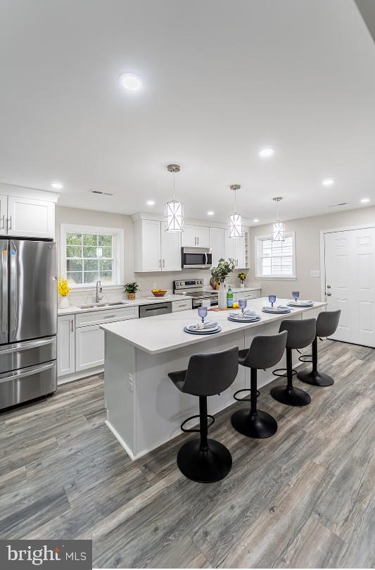 kitchen featuring pendant lighting, sink, appliances with stainless steel finishes, a kitchen island, and white cabinetry