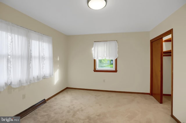 unfurnished bedroom with baseboard heating, light colored carpet, and a closet