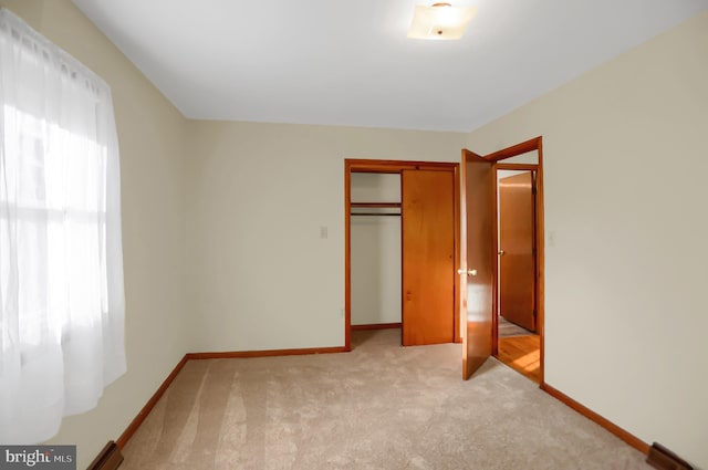 unfurnished bedroom with baseboard heating, light colored carpet, and a closet