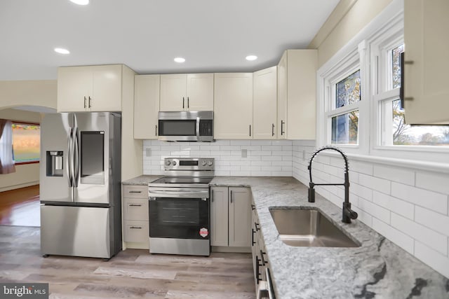 kitchen featuring light hardwood / wood-style flooring, appliances with stainless steel finishes, sink, and light stone counters