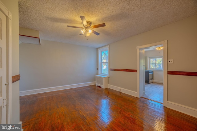 empty room with ceiling fan, a healthy amount of sunlight, a textured ceiling, and dark hardwood / wood-style flooring