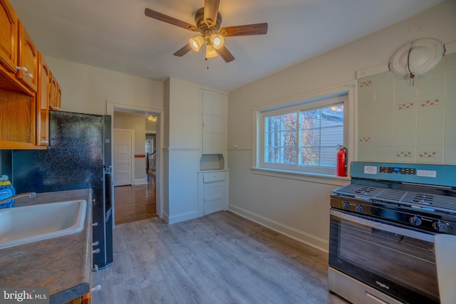 kitchen with ceiling fan, sink, gas range, and light hardwood / wood-style flooring