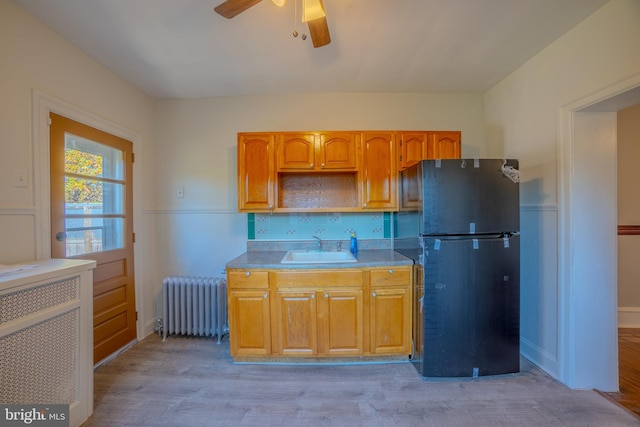 kitchen with sink, tasteful backsplash, radiator, fridge, and light wood-type flooring