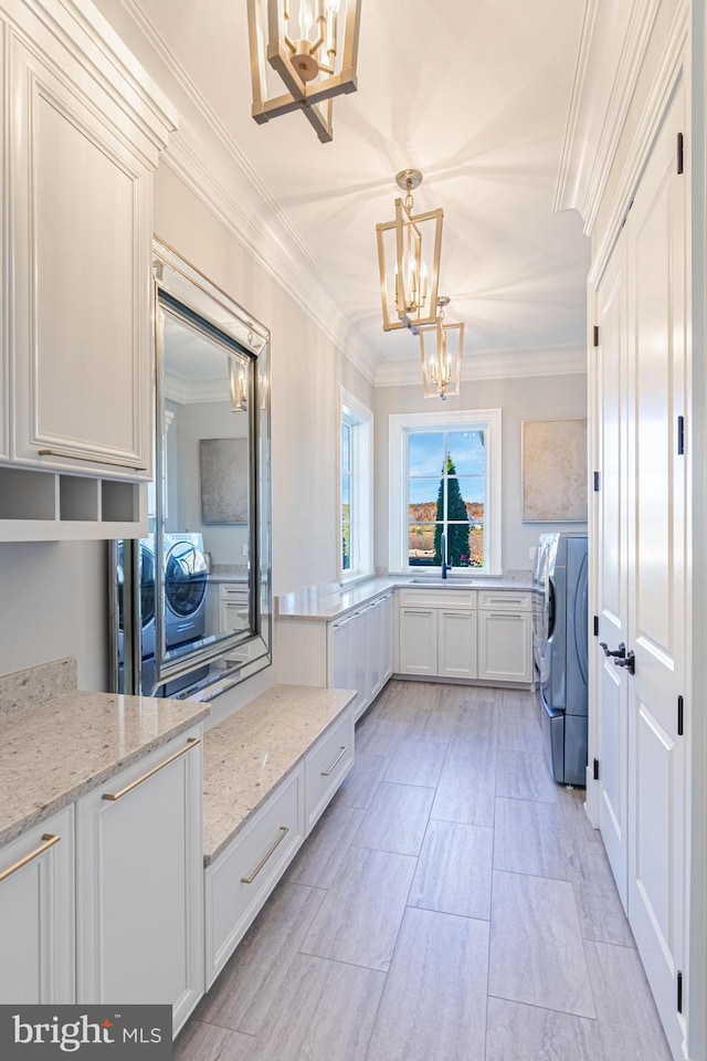 laundry area with an inviting chandelier, cabinets, ornamental molding, and separate washer and dryer