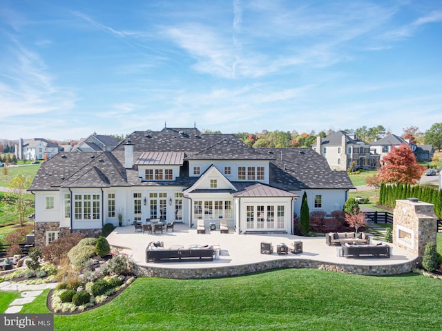 back of property featuring an outdoor living space with a fireplace, french doors, a patio, and a lawn