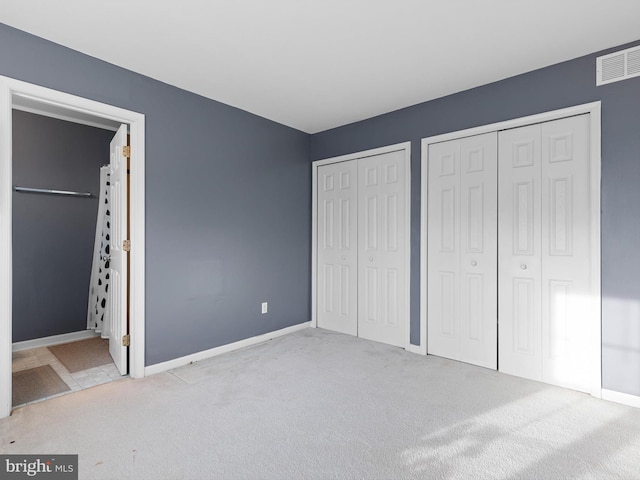 unfurnished bedroom with light colored carpet and multiple closets