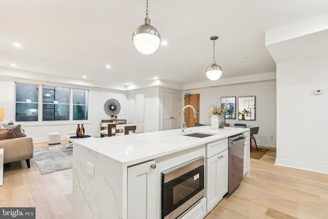 kitchen with stainless steel appliances, a center island with sink, hanging light fixtures, and sink