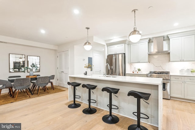 kitchen with wall chimney range hood, hanging light fixtures, sink, and stainless steel appliances