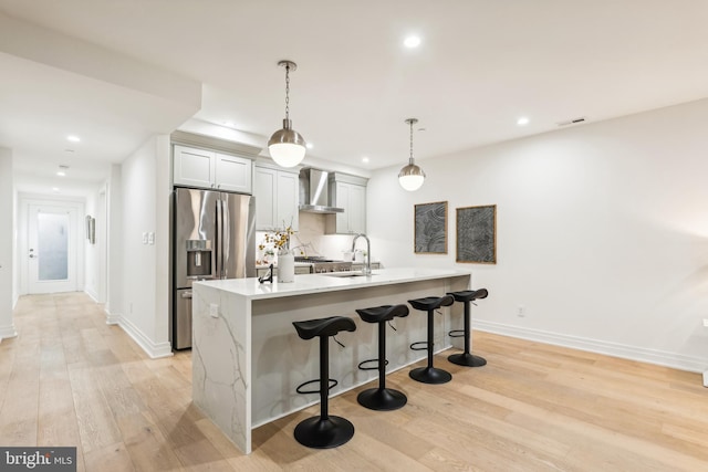 kitchen featuring stainless steel fridge, wall chimney range hood, pendant lighting, sink, and light hardwood / wood-style floors